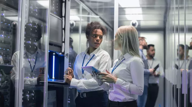 Medium shot of two women working in a data center with rows of server racks and checking the equipment and discussing their work