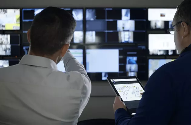 Twee mannen kijken naar verschillende beeldschermen waarop camerabeelden te zien zijn.