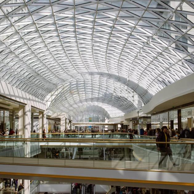 large multi-level shopping mall with various stores, escalators, and visible security measures, including a retail alarm system in place to protect the premises