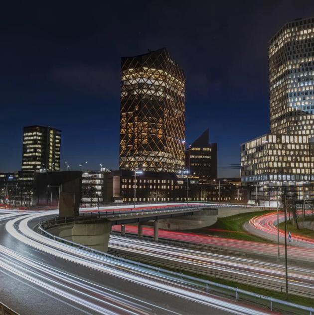 Cityscape at night showing tall office buildings overlooking a road with blurred lines to show moving traffic