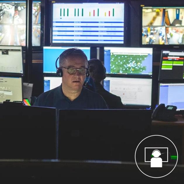 security officer attending to a call inside security monitoring center with multiple video monitoring screens displaying security data 