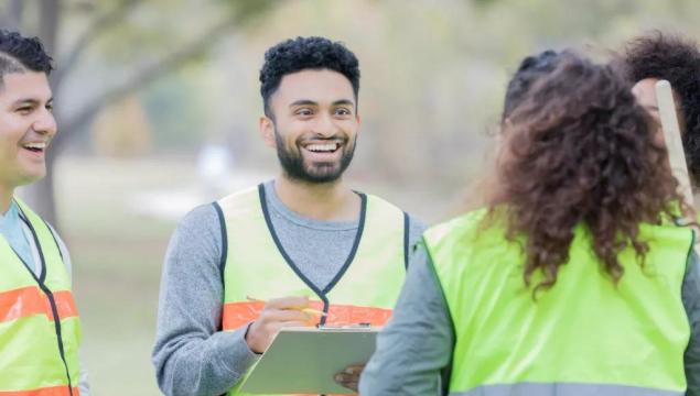 Confident young man talks with a group of male and female community volunteers. He is giving them instructions. They are wearing safety vests.