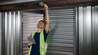 Fire alarm. Serious focused responsible man with tablet checking fire safety adjusting device on garage ceiling